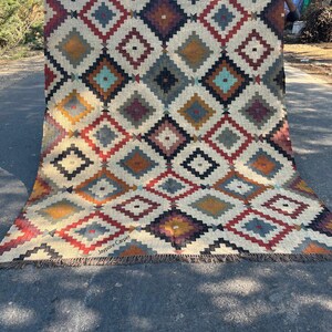May include: A large, rectangular rug with a geometric diamond pattern in shades of red, yellow, blue, and brown on a cream background. The rug has a fringed edge and the text "Jaypore Carpet" is visible.