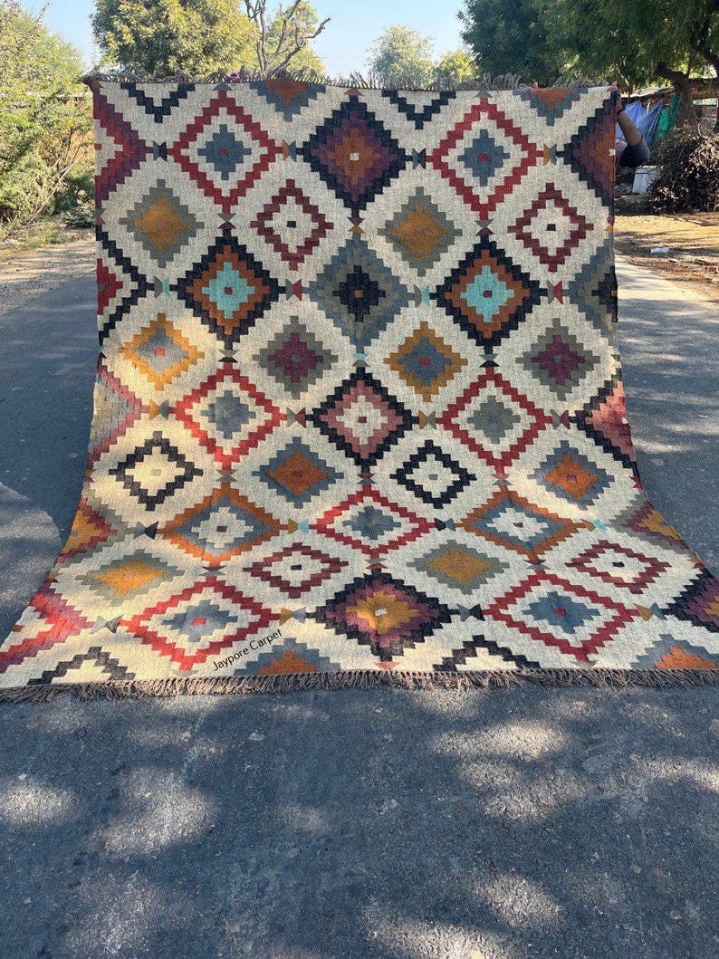May include: A large, rectangular rug with a geometric diamond pattern in shades of red, yellow, blue, and brown on a cream background. The rug has a fringed edge and the text "Jaypore Carpet" is visible.