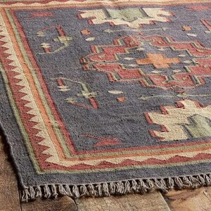 Pode incluir: Um tapete retangular com um padr&atilde;o geom&eacute;trico em tons de cinza, vermelho, laranja, verde e bege. O tapete tem uma borda com franjas e uma borda com um design de tri&acirc;ngulo repetido. O tapete &eacute; feito de um material tecido.