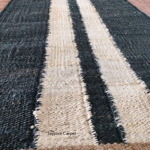 May include: A rolled-up, rectangular rug with a dark blue-gray background and two wide, off-white stripes running lengthwise. The rug has a textured appearance and a brown border. The text "Jaypore Carpet" is visible on the rug.