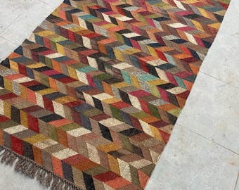 May include: A rectangular rug with a geometric pattern of colorful, interlocking shapes. The rug features a variety of colors, including red, orange, yellow, green, and brown. The edges are finished with a fringe.