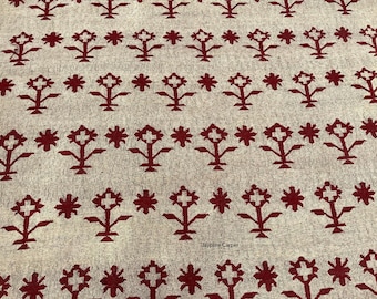 May include: A beige textile with a repeating pattern of stylized floral and star-like shapes in a deep red color. The design is evenly spaced across the fabric, creating a symmetrical and visually appealing pattern. The textile appears to be a rug or carpet.