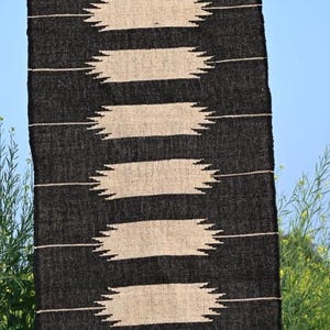 May include: A black and beige woven rug with a geometric pattern. The rug features horizontal beige stripes with jagged edges against a black background. The text "Jaypore Carpet" is visible.