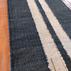 May include: A rectangular rug with a dark blue background and two off-white stripes running lengthwise. The rug has a textured appearance and a fringed edge. The text "Jaypore Carpet" is visible on the rug.