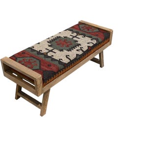 May include: A wooden bench with a rectangular seat featuring a patterned rug design in red, black, green, and cream colors. The bench has a light brown wooden frame and angled legs, suitable for indoor use.