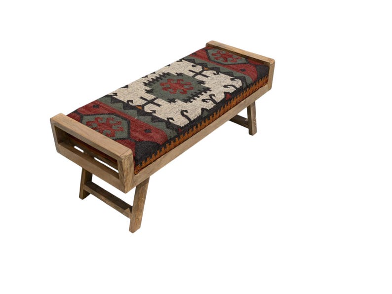 May include: A wooden bench with a rectangular seat featuring a patterned rug design in red, black, green, and cream colors. The bench has a light brown wooden frame and angled legs, suitable for indoor use.