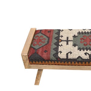 May include: A wooden bench with a rectangular seat featuring a patterned textile in red, gray, black, and cream colors. The bench has a light-colored wooden frame and legs, creating a rustic aesthetic. The seat's design includes geometric shapes.