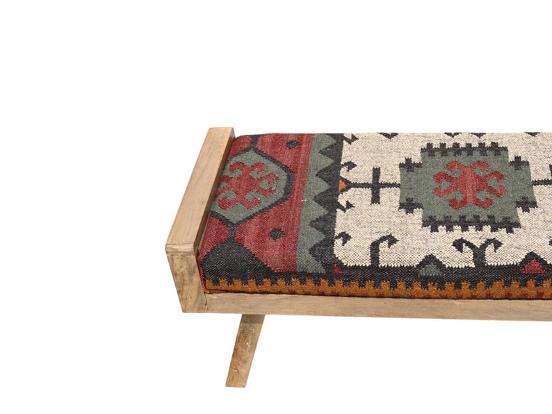 May include: A wooden bench with a rectangular seat featuring a patterned textile in red, gray, black, and cream colors. The bench has a light-colored wooden frame and legs, creating a rustic aesthetic. The seat's design includes geometric shapes.