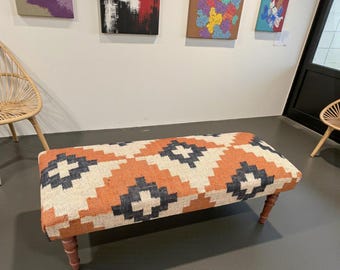 Op de afbeelding: Een rechthoekige bank met een patroonstoffen bovenkant in oranje, crème en marineblauw. De bank heeft vier houten poten. Het stoffen ontwerp heeft geometrische vormen. De bank is een decoratief meubelstuk.