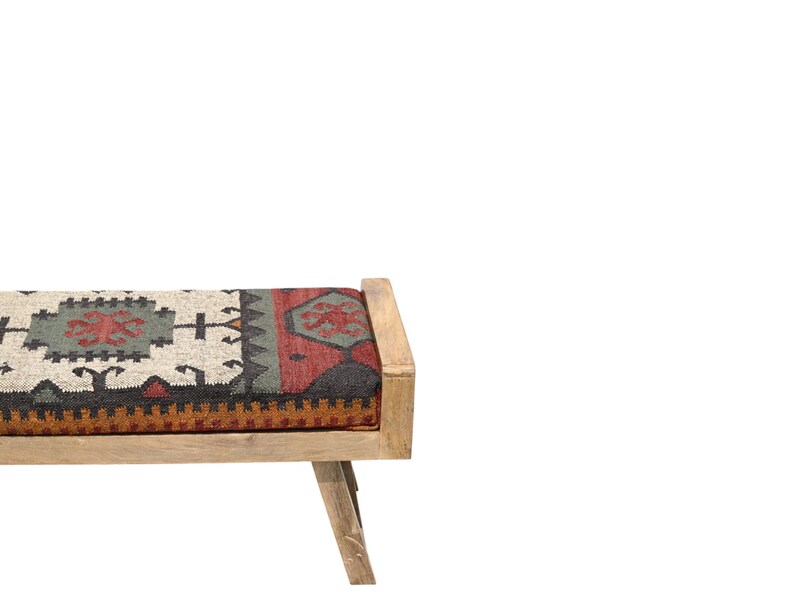 May include: A wooden bench with a rectangular seat featuring a patterned fabric in shades of red, green, black, and beige. The bench has a light-colored wooden frame and angled legs, suitable for indoor use.
