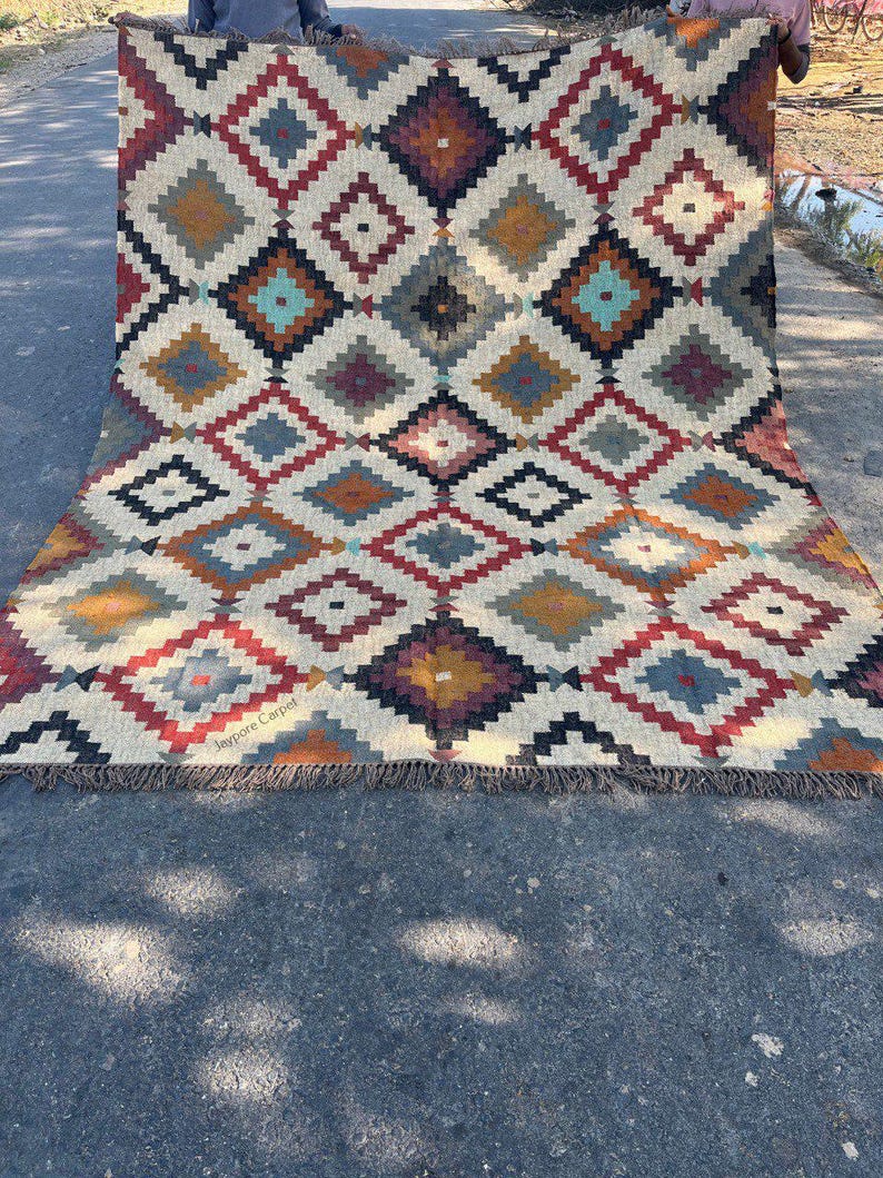 May include: A large, rectangular rug with a geometric diamond pattern in shades of red, blue, yellow, and brown on a cream background. The rug has a fringed edge and the text "Jaypore Carpet" is visible.