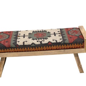 May include: A wooden bench with a rectangular seat featuring a colorful, patterned rug design in red, green, black, and cream. The bench has light-colored wooden legs and armrests, creating a rustic aesthetic.