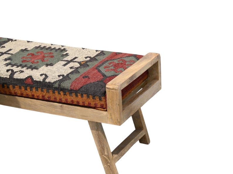 May include: Wooden bench with a rectangular seat featuring a patterned textile in shades of beige, red, green, and black. The bench has a natural wood finish and angled legs, suitable for indoor use.