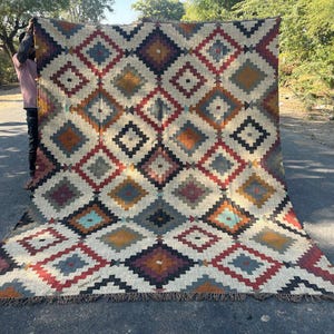 May include: A large, rectangular rug with a geometric diamond pattern in shades of cream, red, blue, orange, and black. The rug has a fringed edge and is displayed outdoors. The text "Jaipur Carpet" is visible on the rug.