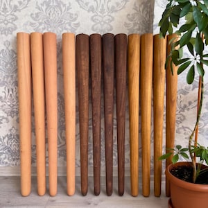 May include: A collection of twelve cylindrical wooden furniture legs arranged in a row, featuring a gradient of finishes ranging from light natural wood tones to medium brown and dark espresso stains, each with a smooth, tapered, and rounded base.