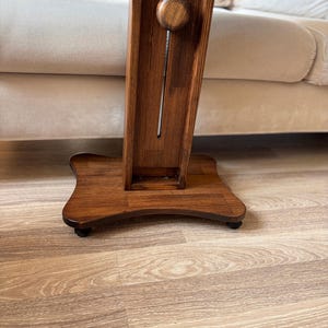 May include: A wooden floor lamp with a dark brown finish. The lamp has a rectangular column with a decorative wooden knob and a square base. The lamp is on a hardwood floor.