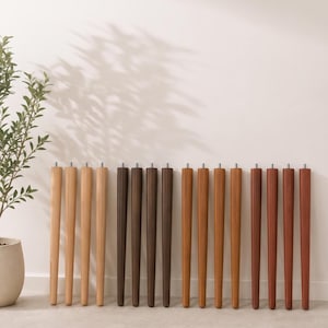 May include: Sixteen tapered wooden furniture legs arranged in four distinct color groups, ranging from light natural wood to dark brown and reddish-brown tones. Each leg features a smooth cylindrical shape and a small metal bolt at the top end.