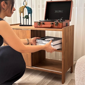 May include: A wooden cabinet with a vintage record player and a stack of Chanel books. The record player is in a brown case. A decorative sculpture of three giraffes is on top of the cabinet.