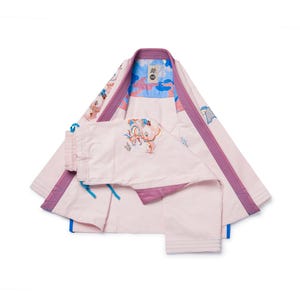 Könnte beinhalten: Ein hellrosa Kampfsportanzug mit lila Besatz und gestickten Details. Die Uniform besteht aus einer Jacke und einer Hose mit blauem und gemustertem Innenfutter. Die Jacke hat einen Kragen und die Hose hat einen Kordelzug.