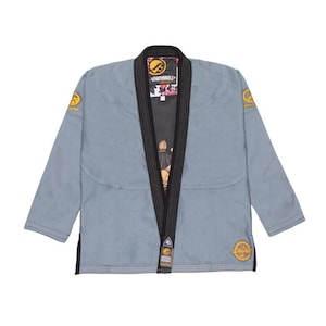 Pode incluir: Um gi de artes marciais azul claro com acabamentos pretos e detalhes dourados. O gi apresenta o nome da marca "Shoyoroll" na gola e nos patches. O forro interior tem um design floral. Este uniforme é projetado para treinamento e competição de artes marciais.