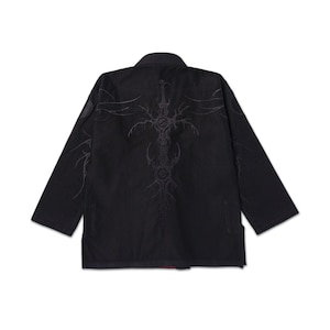 Puede incluir: Uniforme negro de artes marciales con un diseño decorativo en la espalda. El diseño es una cruz gris oscuro estilizada con detalles intrincados. El uniforme tiene mangas largas y cuello.