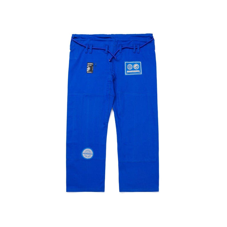 May include: Bright blue martial arts pants with a drawstring waist. The pants have several patches and logos, including a circular patch on the lower left leg and rectangular patches near the waist. The fabric appears to be a durable, woven material.