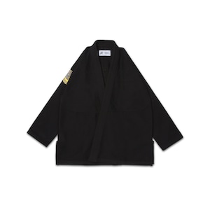 Pode incluir: Uniforme preto de artes marciais com gola em V e mangas compridas. O uniforme tem um patch no ombro esquerdo com detalhes amarelos e brancos. O uniforme está estendido sobre uma superfície branca.