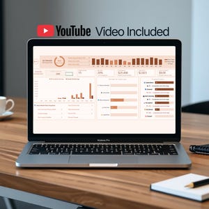 May include: A silver MacBook Pro laptop displaying a data analytics dashboard with charts and graphs. The screen shows financial data, including percentages and dollar amounts. The text "YouTube Video Included" is at the top. The laptop is on a wooden desk.