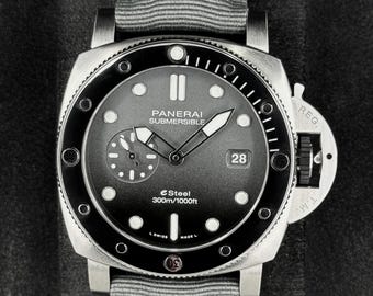 May include: A stainless steel Panerai Submersible watch with a gray fabric strap. The watch face is black with white markers, a date display, and the text "Panerai Submersible". The watch is water resistant to 300m/1000ft.