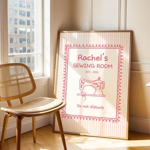 May include: A framed sign with the text "Rachel's SEWING ROOM EST. 2005" in pink, featuring a sewing machine illustration. The sign has a pink and white striped background and a decorative pink border. The words "Do not disturb" are at the bottom.
