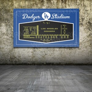 Puede incluir: Un marcador de estilo vintage con el texto "Dodger Stadium" y "Los Angeles Dodgers" en letras doradas sobre un fondo azul. El marcador muestra estad&iacute;sticas de b&eacute;isbol, incluyendo promedios de bateo, jonrones, carreras impulsadas, porcentaje de embasamiento, porcentaje de slugging y el marcador del juego. El marcador tambi&eacute;n muestra el n&uacute;mero de bolas, strikes y outs.