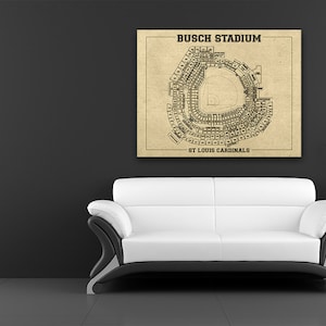 Puede incluir: Una impresión enmarcada del Busch Stadium, hogar de los Cardenales de San Luis, cuelga sobre un sofá blanco y negro. El diseño del estadio se representa en un esquema detallado en tonos sepia. Las palabras "BUSCH STADIUM" y "ST LOUIS CARDINALS" están impresas.