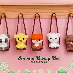 May include: Five crocheted animal toys, including a panda, fox, bear, and cat, each seated in a swing. The swings are suspended from a wooden shelf. The text "Animal Swing Set PDF Pattern" is displayed below the swings.