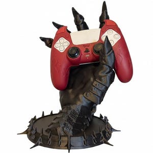 Könnte beinhalten: Ein roter Videospiel-Controller ruht in einem schwarzen, krallenartigen Halter. Der Controller hat weiße Knöpfe und ein PlayStation-Logo. Der Halter hat einen stacheligen Sockel und ein detailliertes, strukturiertes Design, ein einzigartiges Gaming-Zubehör.