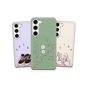 Puede incluir: Tres fundas para teléfono con ilustraciones de zapatos. Una es de color lila claro con zapatillas negras y granates, otra es verde con burbujas de diálogo "HI", y la última es blanquecina con zapatillas blancas.