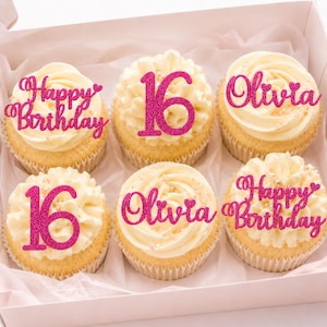 May include: Six cupcakes with white frosting in a box, each topped with a pink glittery cake topper. The toppers feature the text Happy Birthday, the number 16, or the name Olivia, all written in a cursive or bold font with small heart accents.