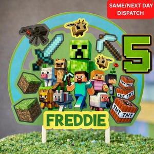 May include: A Minecraft cake topper with a green and blue design, featuring character figures, blocks, and the number 5. The name "FREDDIE" is displayed on a green banner. The text "SAME/NEXT DAY DISPATCH" is in a red box.