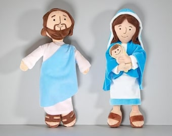 May include: Two plush dolls: one depicting a man with a beard in a blue robe, and the other a woman in a blue veil holding a baby. Both dolls have brown sandals and are set against a gray background.