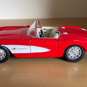 Op de afbeelding: Een rood en wit schaalmodel van een cabriolet met een glanzende rode carrosserie, een wit zijpaneel met een klein embleem, een doorzichtige voorruit en een beige interieur. Het voertuig heeft zilverkleurige wielen met zwarte banden.