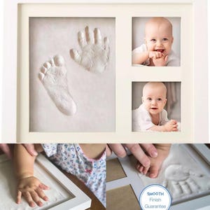 May include: A white framed baby keepsake kit. The kit includes a space for a handprint and footprint, and two photo slots. The handprint and footprint are white. The photos show a smiling baby. The frame has a smooth finish.