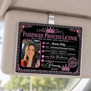 Peut inclure: Un accessoire de pare-soleil de voiture noir rectangulaire avec une bordure à paillettes roses et des icônes de cœur. Il affiche le texte Passenger Princess License, une photo d'une personne et des champs pour le nom, le titre et le statut.