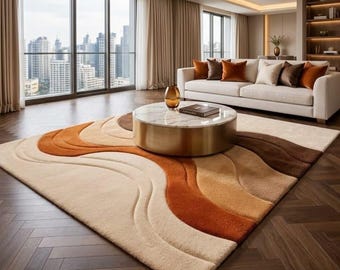 May include: A rectangular area rug featuring a textured, wavy pattern in shades of cream, tan, and burnt orange. The rug is placed on a dark wood floor in front of a round coffee table with a white marble top and a gold metal base.