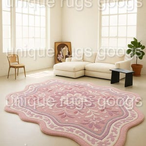 Può includere: Un tappeto rosa e bianco a motivi floreali con un bordo ondulato unico. Il tappeto è posto in una stanza luminosa con un divano bianco, un tavolino nero e una pianta in vaso. Il design del tappeto presenta un motivo floreale centrale.