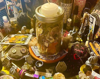 Puede incluir: Un surtido de artículos espirituales y metafísicos, que incluyen velas, cartas del tarot y frascos llenos de hierbas. Un gran tarro con una vela encima es el punto focal, rodeado de otros objetos rituales.