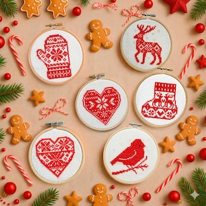May include: A collection of Christmas-themed cross-stitch embroidery hoops. Designs include a mitten, reindeer, heart, stocking, and bird, all in red on white fabric. The hoops are surrounded by gingerbread cookies, candy canes, and ornaments.