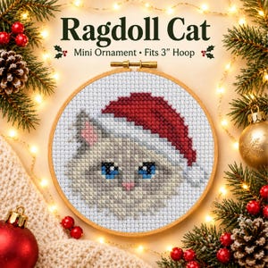 May include: A cross-stitch pattern of a Ragdoll cat wearing a red Santa hat, displayed in a wooden embroidery hoop. The text reads Ragdoll Cat Mini Ornament Fits 3" Hoop. The cat has light fur, blue eyes, and a pink nose on white fabric.