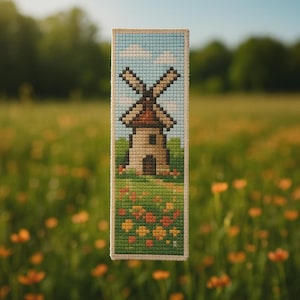 May include: A cross-stitched bookmark featuring a windmill scene. The design includes a blue sky with clouds, a brown-roofed windmill, green grass, and colorful flowers. The bookmark is rectangular with a cream-colored border.