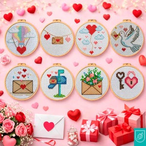 Può includere: Una collezione di otto cerchi da ricamo a punto croce con temi di San Valentino. I disegni includono cuori, buste, una cassetta delle lettere, una colomba e una chiave e un lucchetto. I cerchi sono disposti su uno sfondo rosa con cuori e regali decorativi.