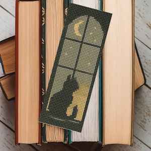 May include: A handmade bookmark depicting a black cat silhouette looking out of a window at a crescent moon and stars. The bookmark is set against a backdrop of vintage books with aged, textured covers, creating a cosy, literary aesthetic.