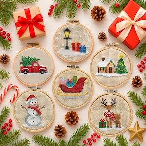 May include: A collection of seven Christmas-themed cross-stitch embroidery hoops. Designs include a red truck with a Christmas tree, a snowman, a reindeer, a sleigh, a house, a lamp post, and wrapped gifts. The hoops are surrounded by pine needles, berries, and gifts.